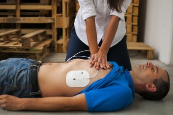 Woman practicing CPR on prone man wearing AED patches
